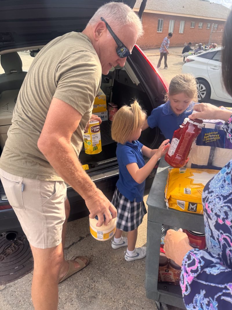 Volunteer helping children carry groceries provided through Open Eyes
